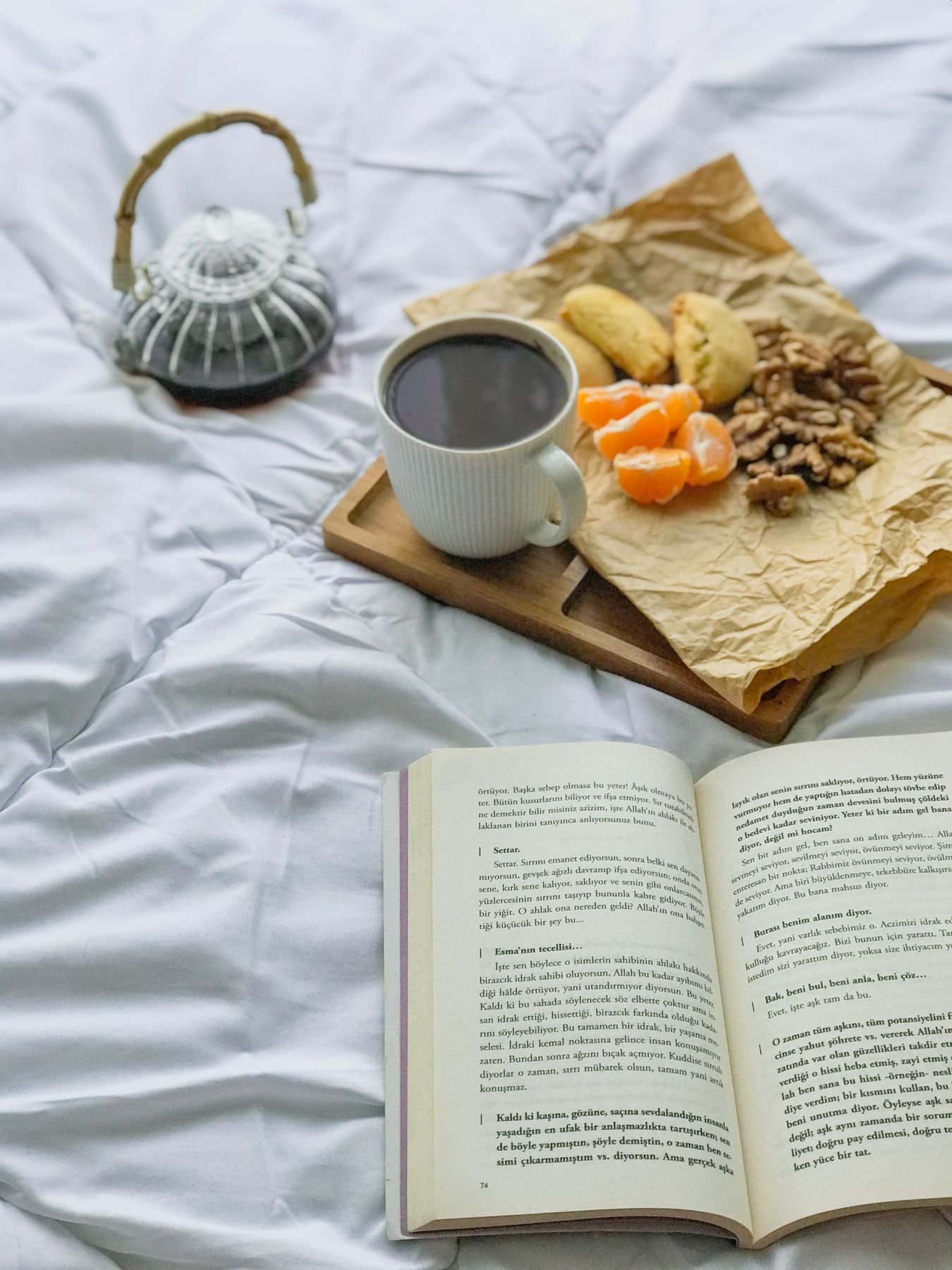 Plateau avec café, biscuits et fruits posé sur un lit, près d’un livre ouvert